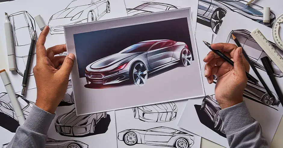 a person looking at car sketches and a photograph of a car at a messy table