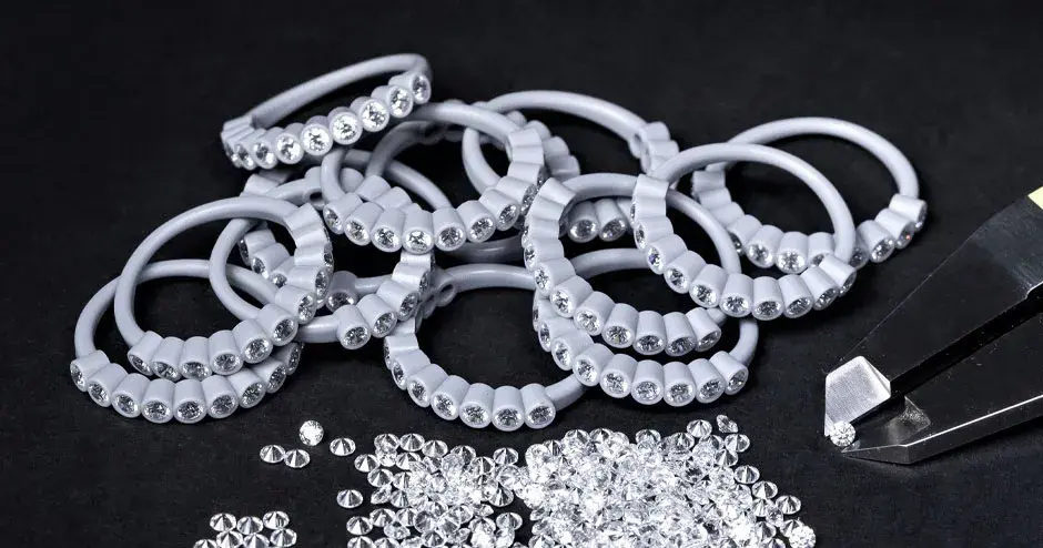 many wax molded rings with diamonds set in, tip of caliper holding a diamond, scattered diamonds