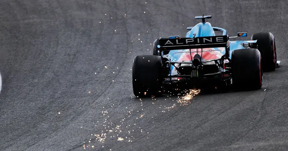 alpine f1 race car on track driving away with sparks coming out of the rear of the car