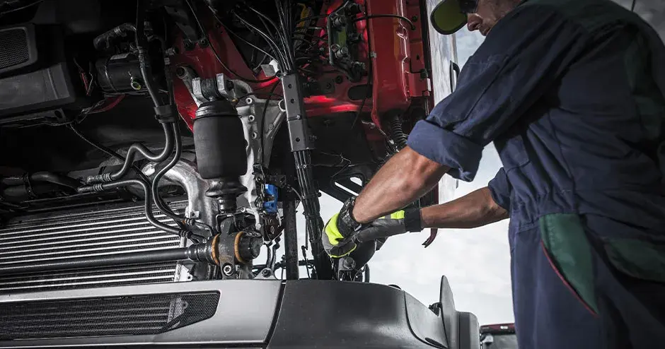 A technician installing a service part under the operator cab of commercial truck.