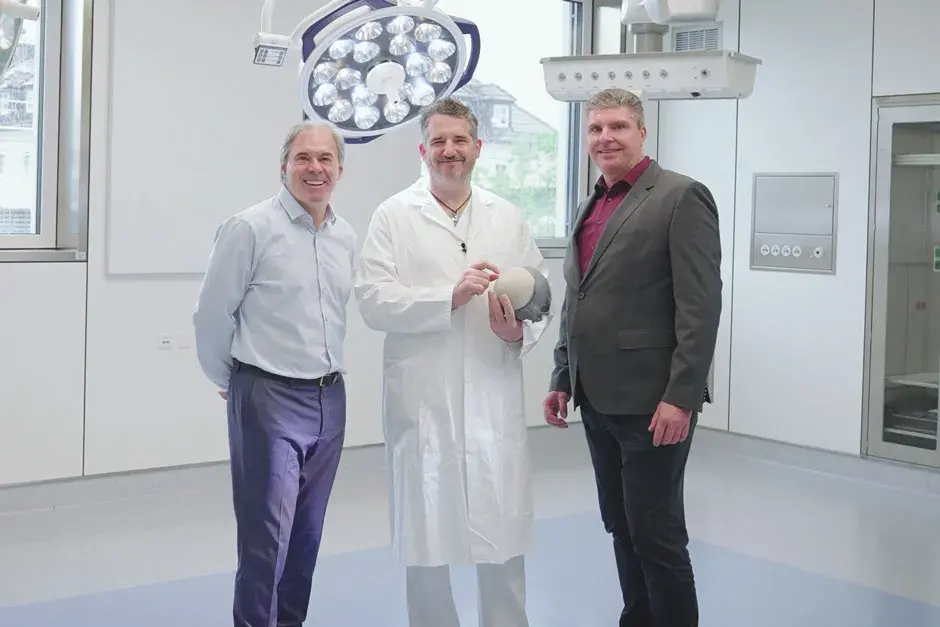3 people, including one doctor, standing in an operating room while the doctor holds a 3D printed implant.